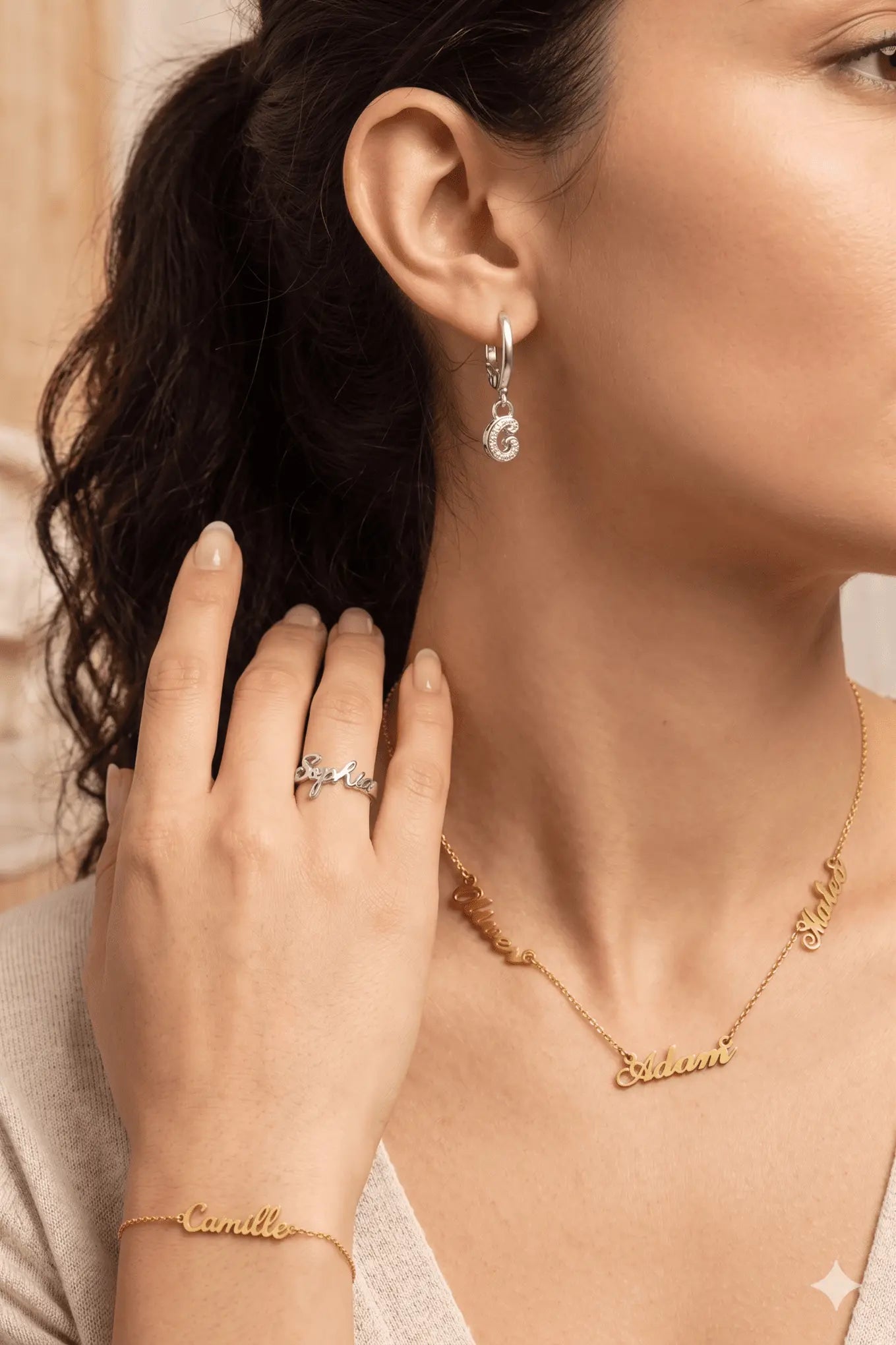 Portrait de femme avec bijoux prénoms personnalisés : collier multi-prénoms doré, bracelet fin avec prénom, bague argentée ciselée et créoles avec pendentif lettre.